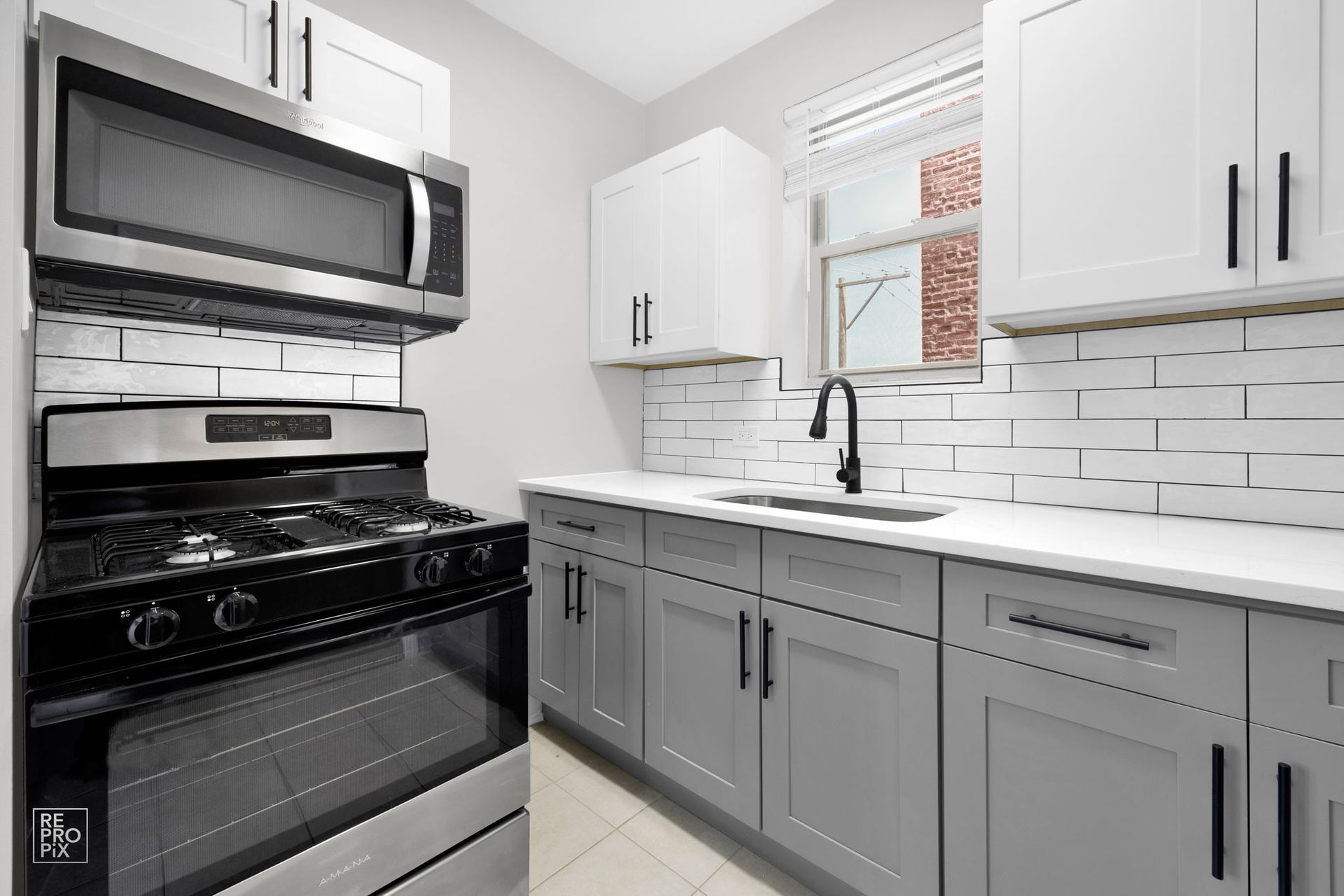 Modern kitchen with grey cabinets, white countertops, stainless steel appliances, and subway tile backsplash.