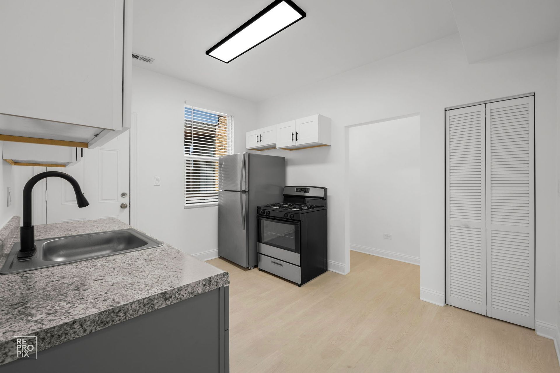 Kitchen with gray cabinets, stainless steel appliances, and light wood floors.