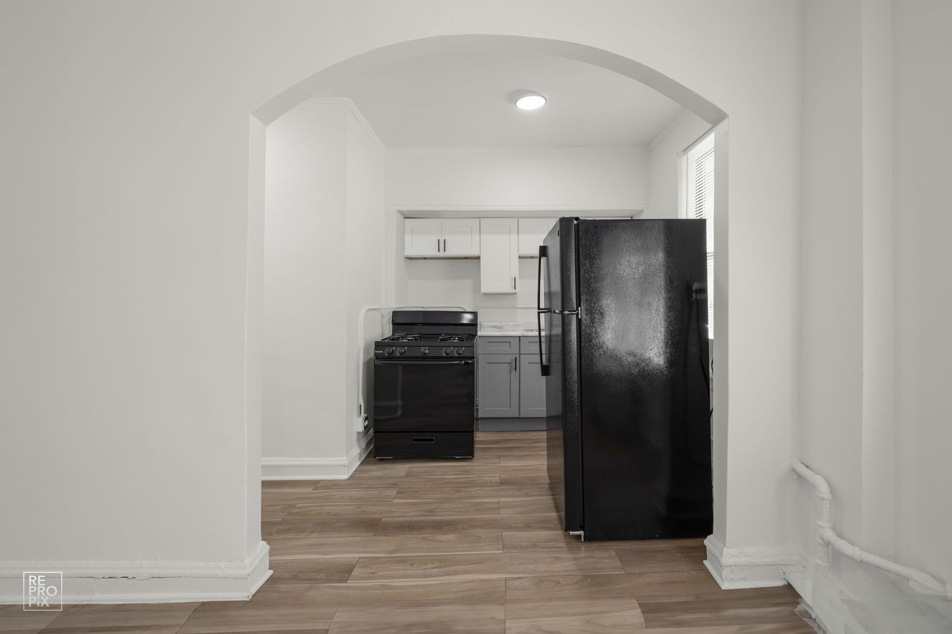View from an archway into a small kitchen with a black refrigerator and stove.