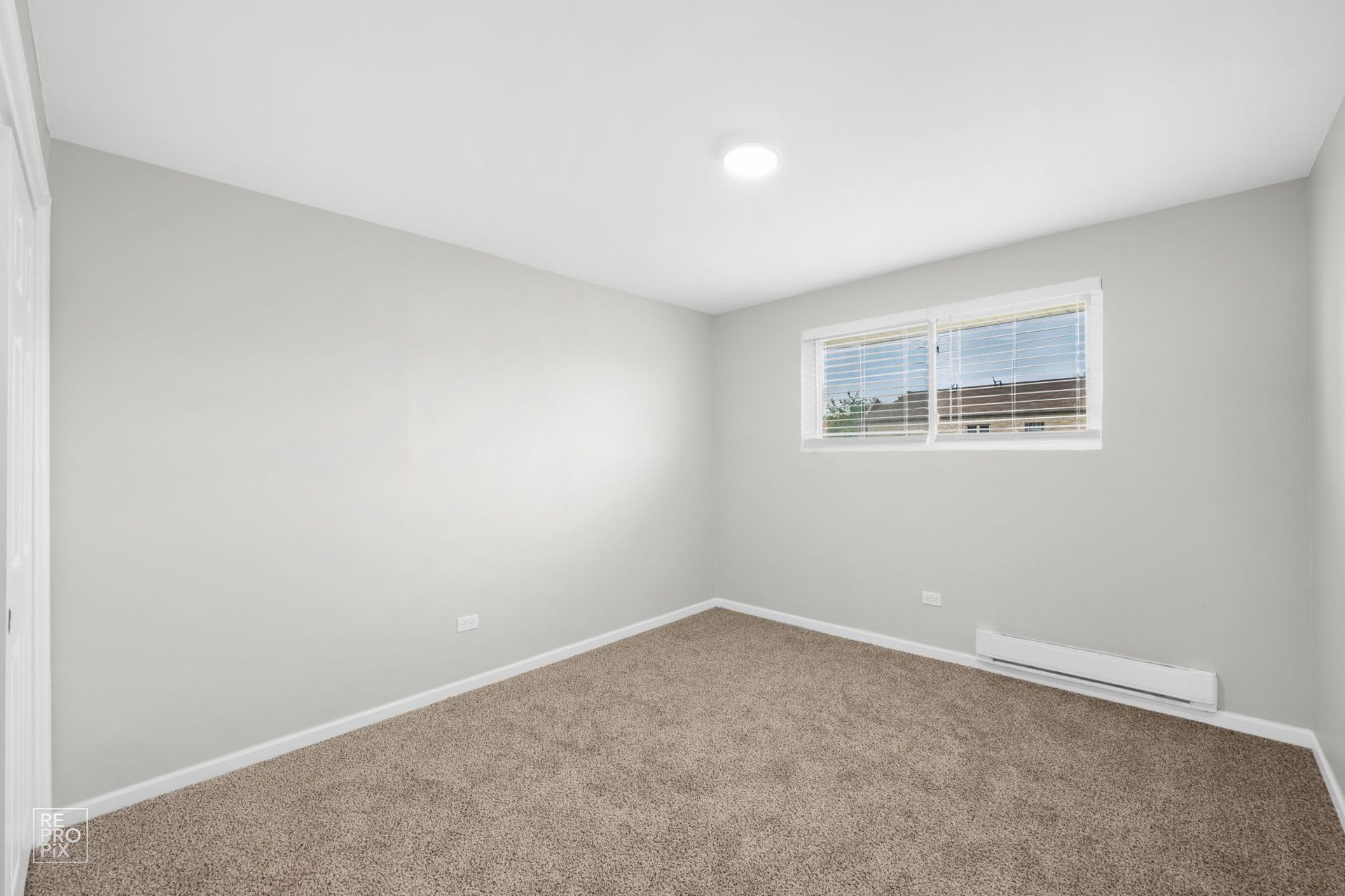 Empty room with gray walls, window, and brown carpet.