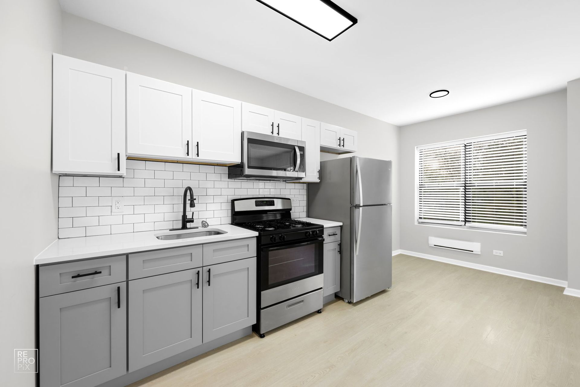 Kitchen with gray and white cabinets, stainless steel appliances, and a window with blinds.