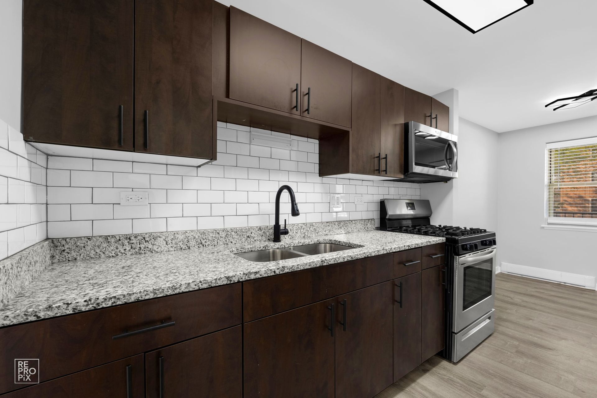 Dark brown kitchen cabinets, stainless steel appliances, white subway tile backsplash, and light granite countertops.
