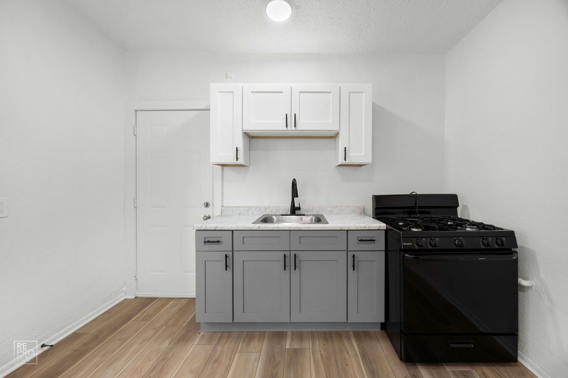 Small kitchen with gray and white cabinets, black stove, and light wood floors.