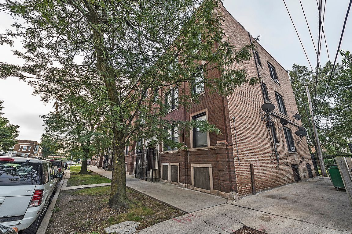 Brick multi-story building with tree in front; sidewalk and street with parked cars visible.