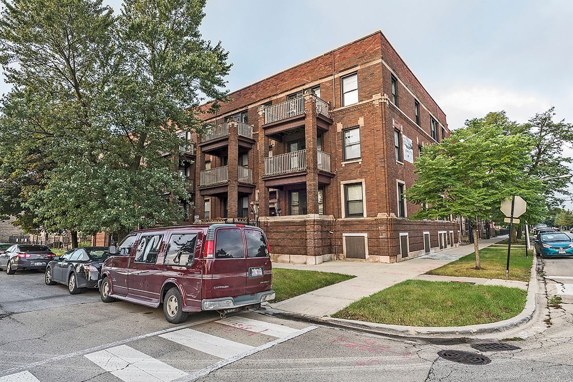 Brick apartment building on a corner lot; a maroon van is parked in front.