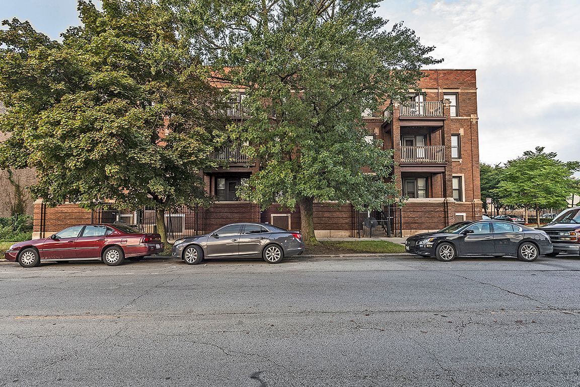 Cars parked in front of a brick apartment building with trees.