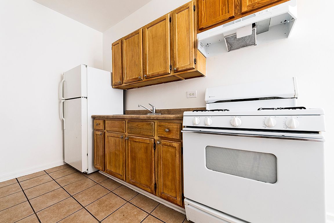 Kitchen with wooden cabinets, white appliances, and tiled floor.