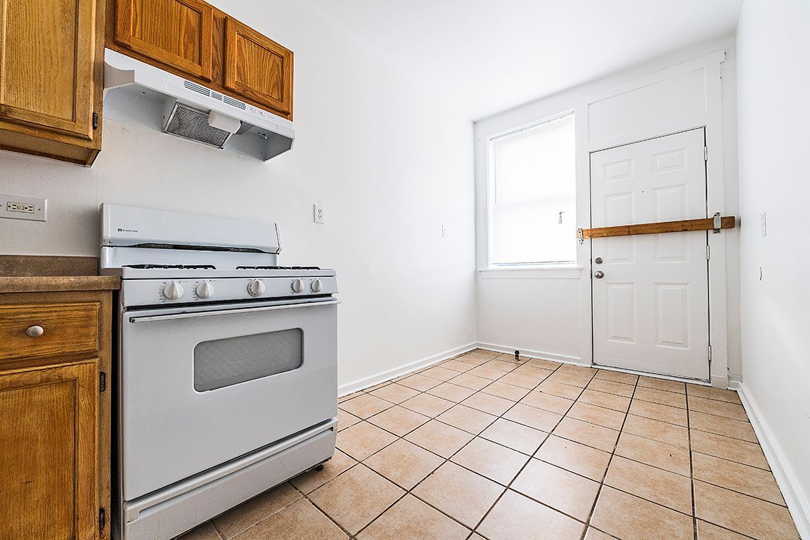 Kitchen with light brown cabinets, white stove, and tile floor. Door and window provide natural light.