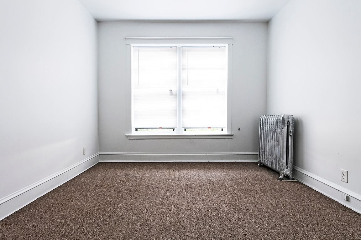 Empty room with brown carpet, window, and radiator.