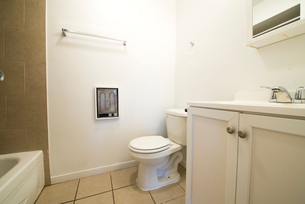 Bathroom with toilet, vanity, and shower/tub combo. Beige tile floor and off-white walls.