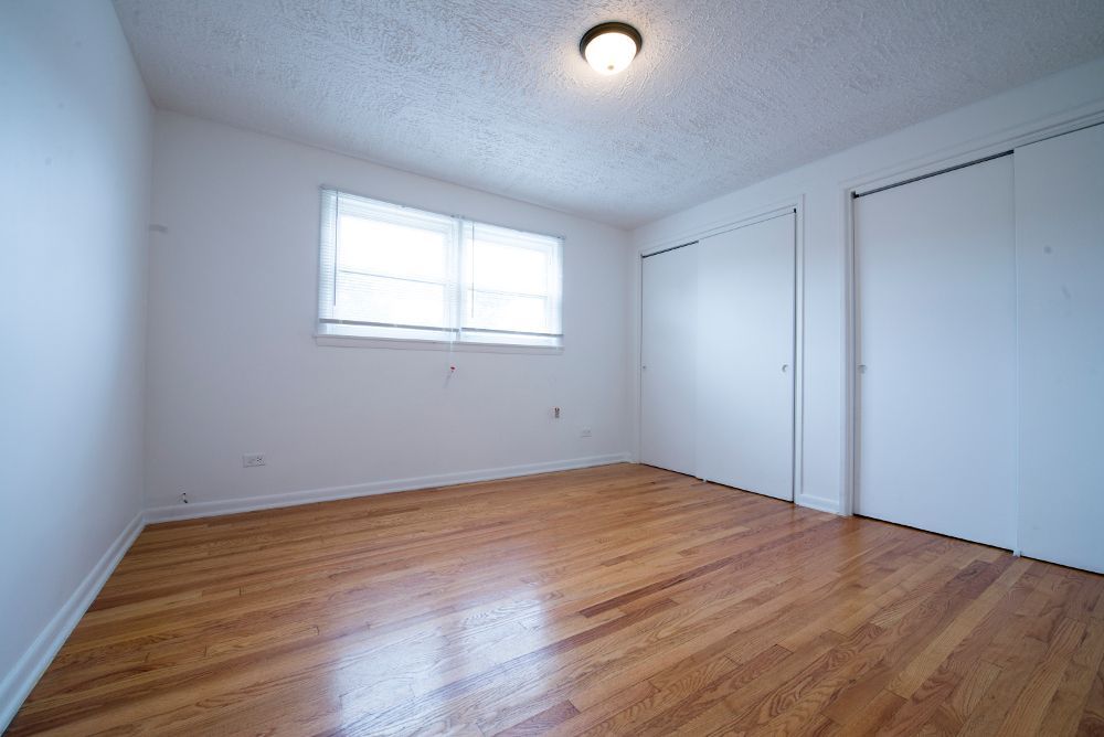 Empty room with hardwood floors, white walls, two closets, and a window.