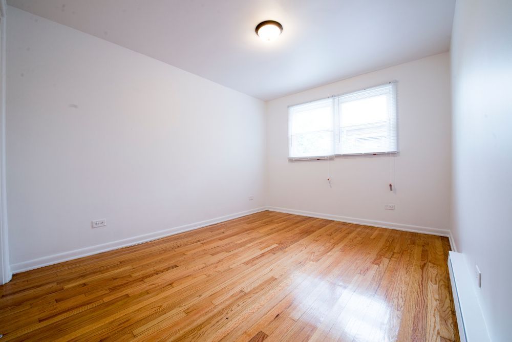 Empty room with hardwood floors, white walls, and a window with blinds.
