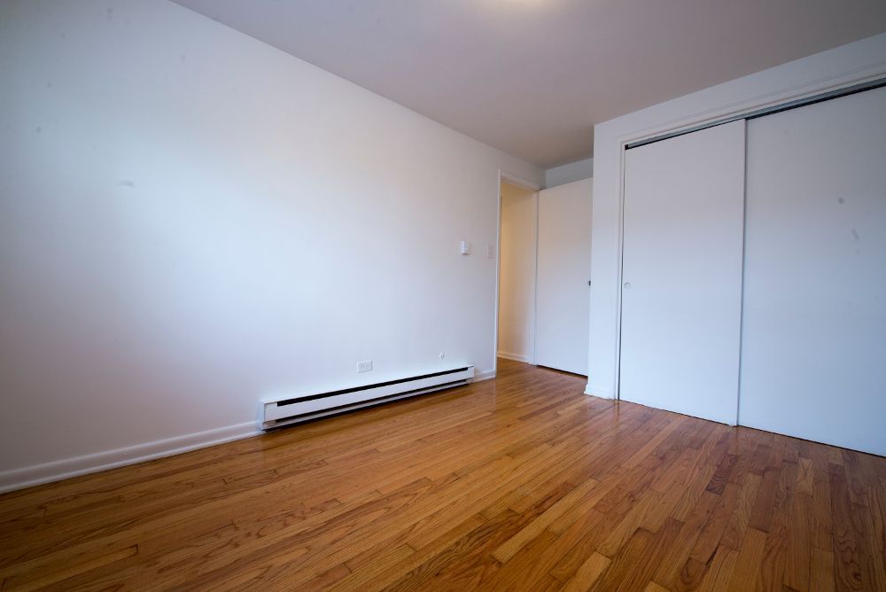 Empty room with hardwood floors, white walls, closet, and baseboard heater.
