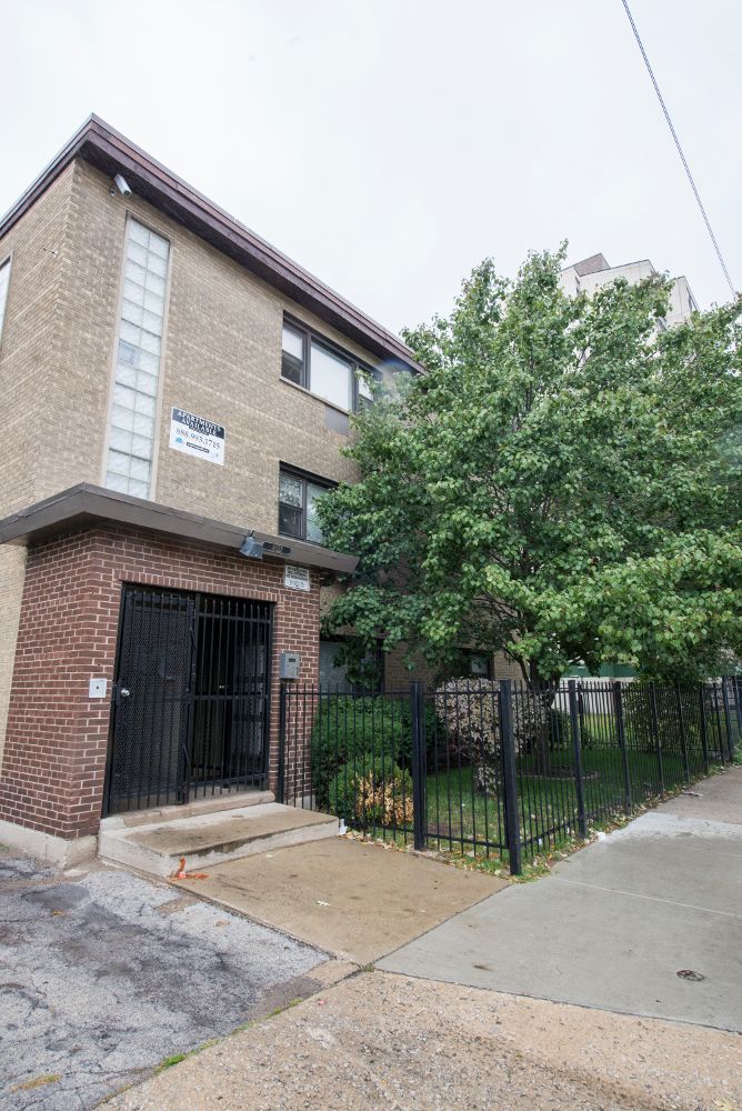 Two-story brick apartment building with black security gate and small green yard, gray sky.