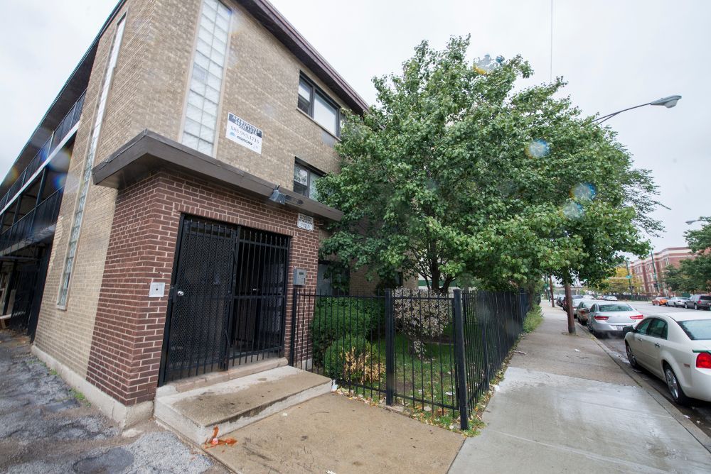 Brick apartment building with black metal gate and sidewalk with parked cars.