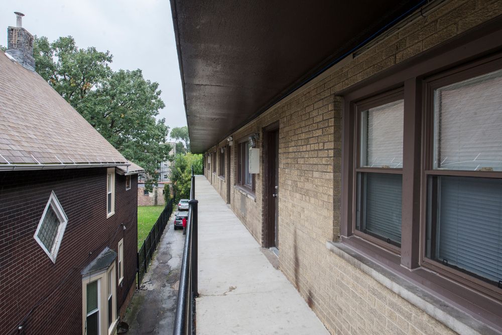 Exterior apartment hallway with brick wall, brown trim, and a narrow walkway.