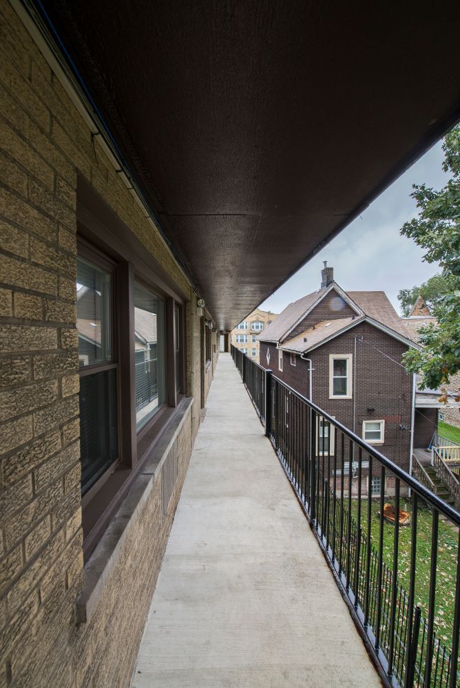 Long, narrow outdoor walkway with railing, dark ceiling, and brick building.