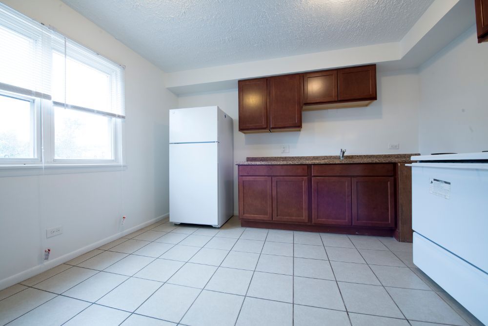 Empty kitchen with brown cabinets, white appliances, and tiled floor.
