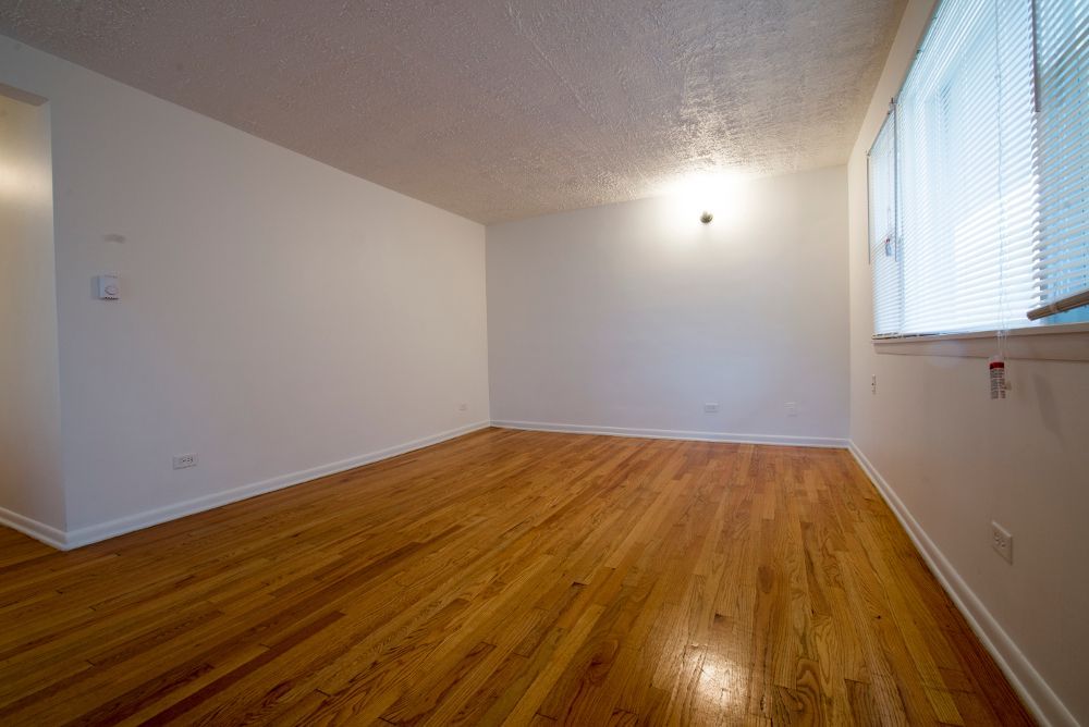 Empty room with hardwood floors, white walls, and a window with blinds.
