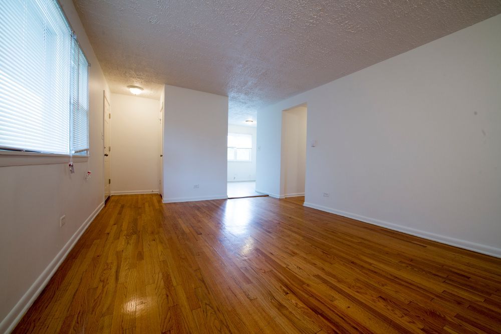 Empty room with hardwood floors, white walls, and a window with blinds.