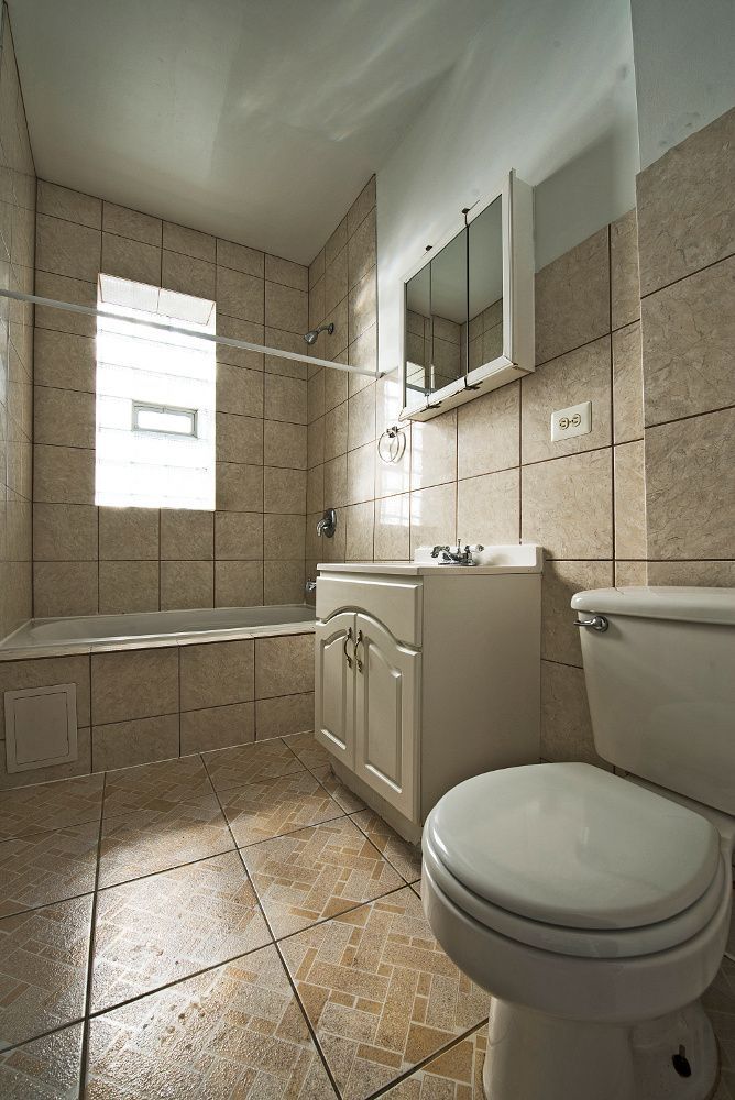 Bathroom with beige tile, white vanity, toilet, and a window above the bathtub.