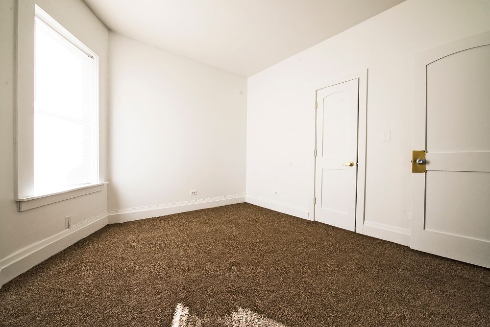 Empty room with brown carpet, white walls, two doors, and a window.