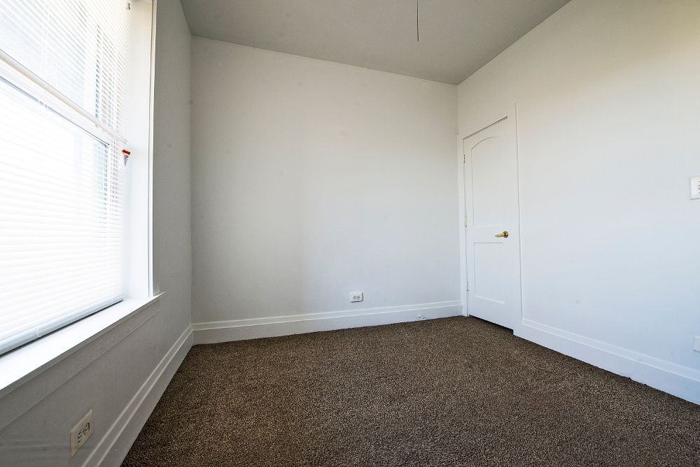 Empty room with window, door, and brown carpet. White walls and trim.