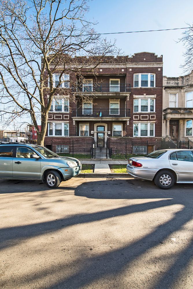 A three-story brick apartment building with cars parked on the street.