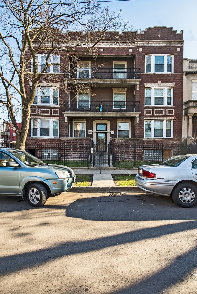 Brick apartment building with balconies, cars parked on street.