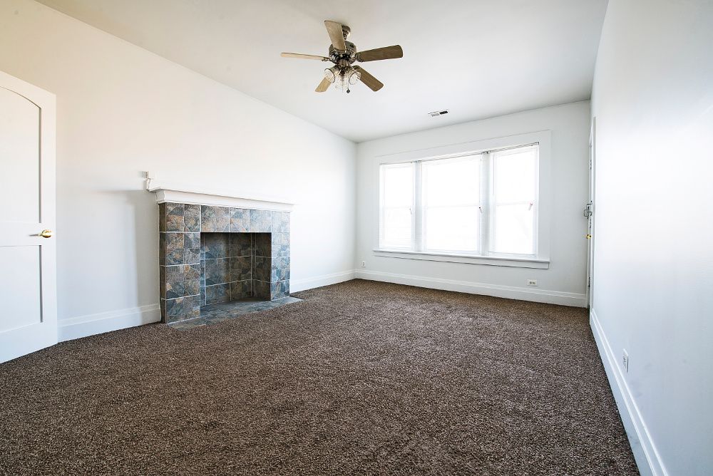 Empty room with brown carpet, fireplace, and windows.