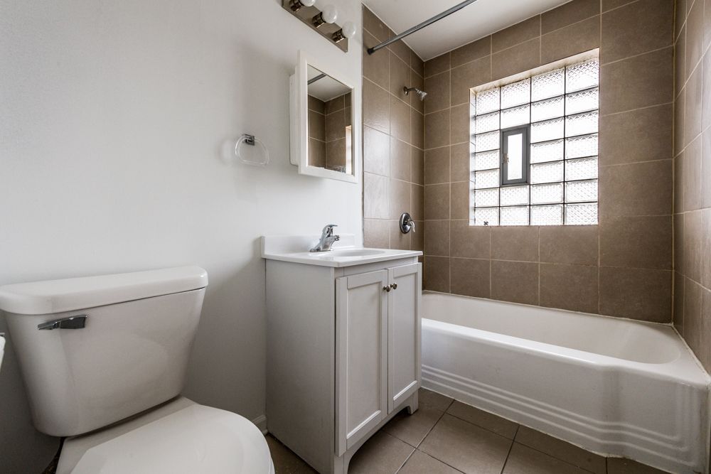 Bathroom with white fixtures, beige tile, and a glass block window.