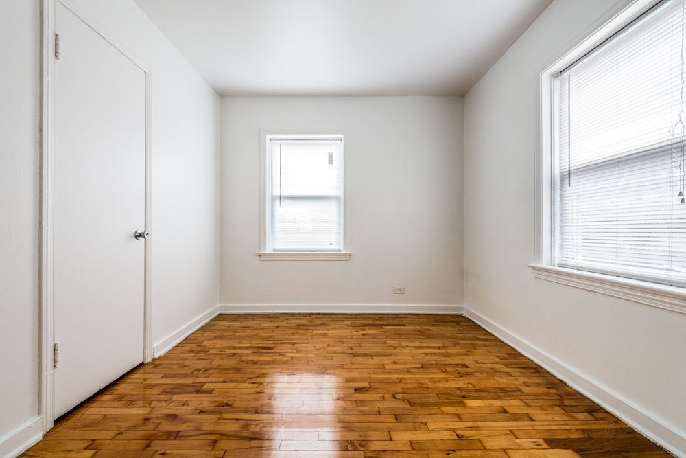 Empty room with wooden floor, white walls, two windows, and a closed door.