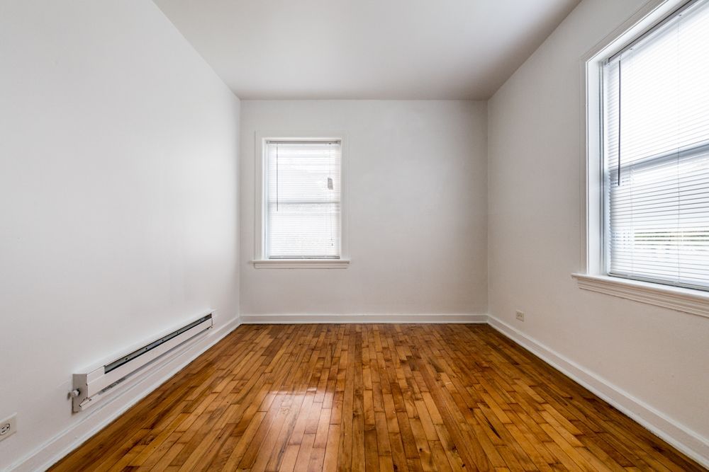 Empty room with hardwood floors, two windows with blinds, and white walls.
