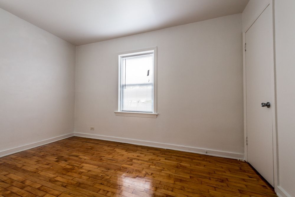 Empty room with wood floor, white walls, small window, and closed door.
