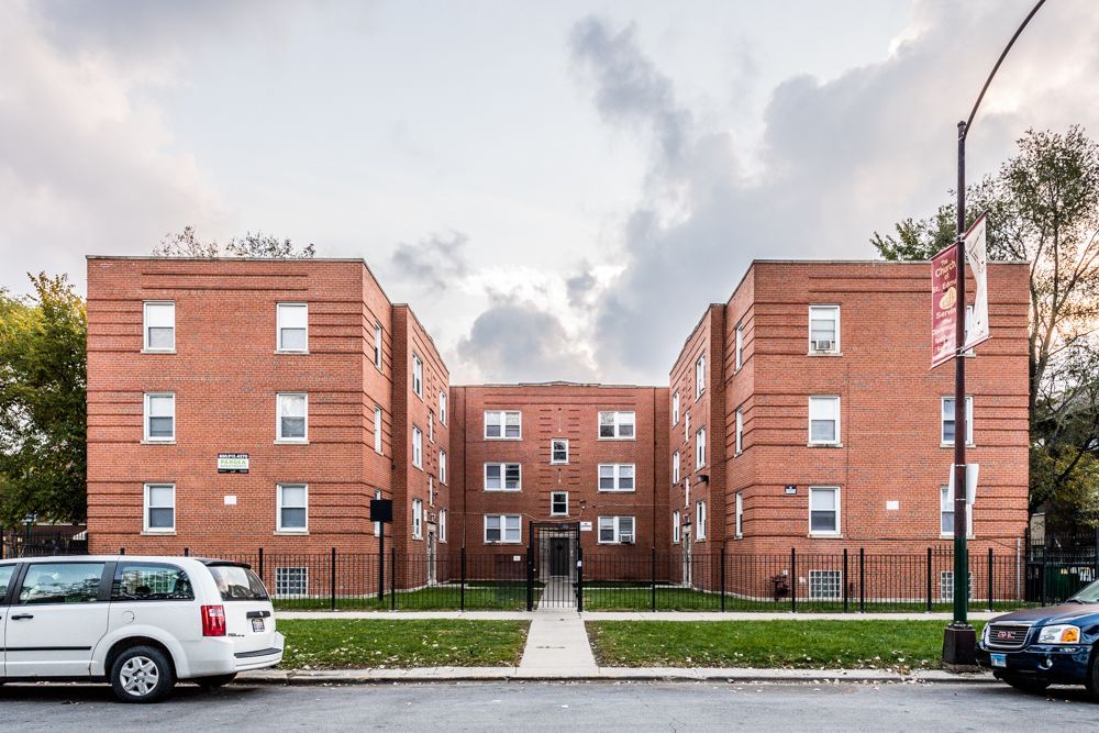 Brick apartment buildings with white-framed windows, a central walkway, and a van parked on the street.