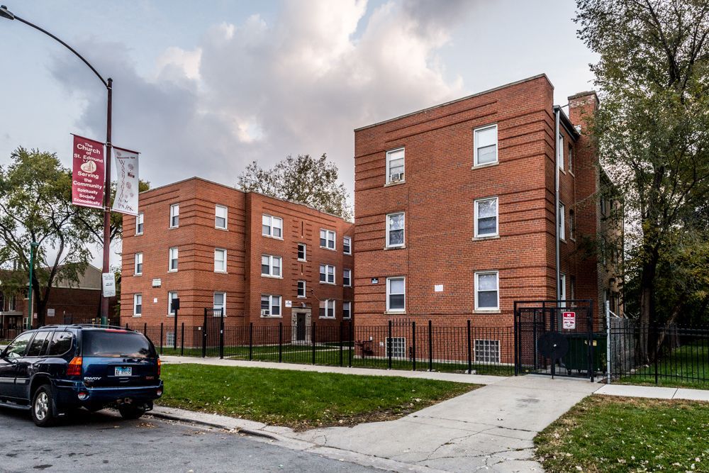 Red brick apartment buildings with black fences and a parked SUV on a city street.