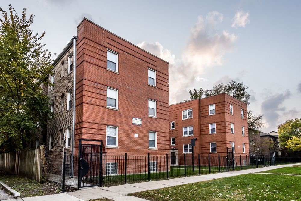 Red brick apartment buildings with black fences and a sidewalk.