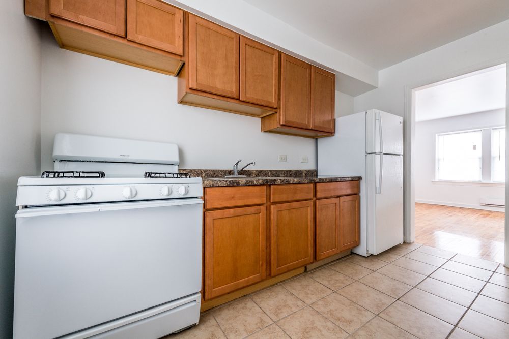Kitchen with white appliances, brown cabinets, and beige tile floor.