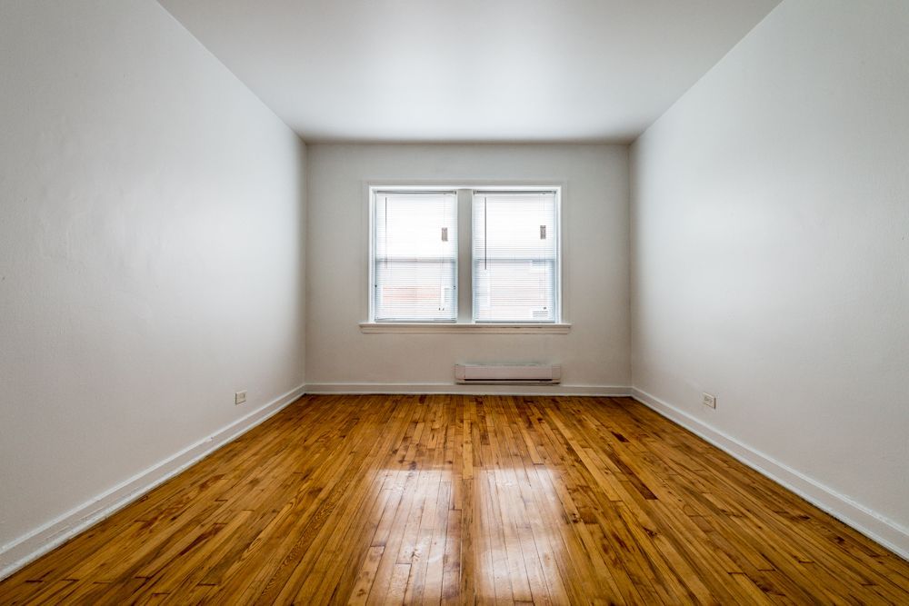 Empty room with wood floors, white walls, and a window with blinds.