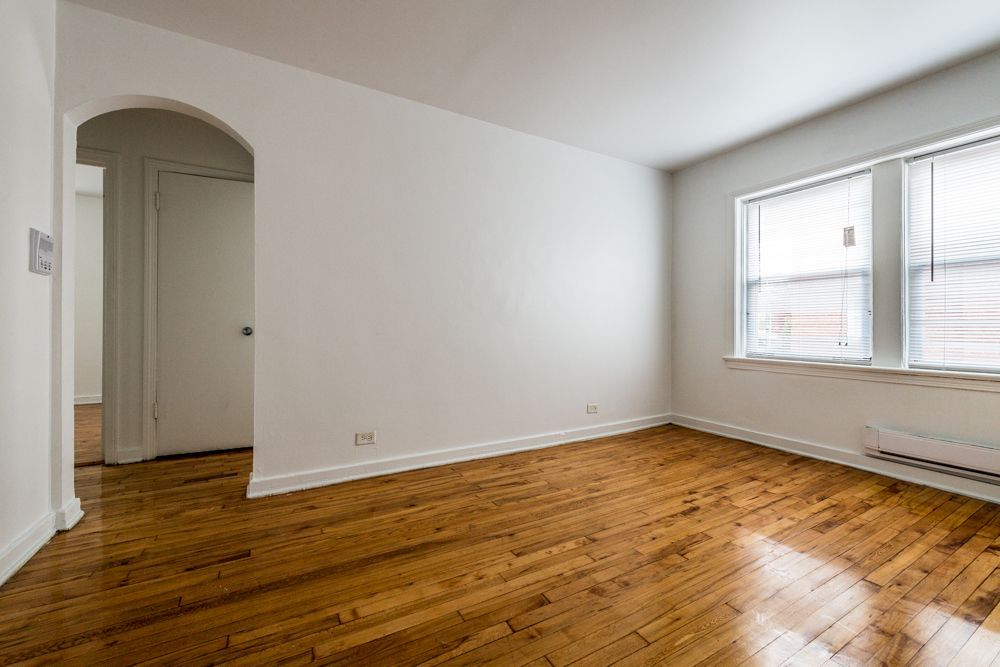 Empty room with hardwood floors, white walls, arched doorway, and a window with blinds.