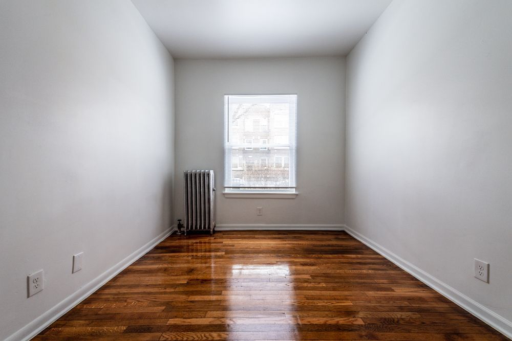 Empty room with hardwood floors, white walls, window, and radiator.