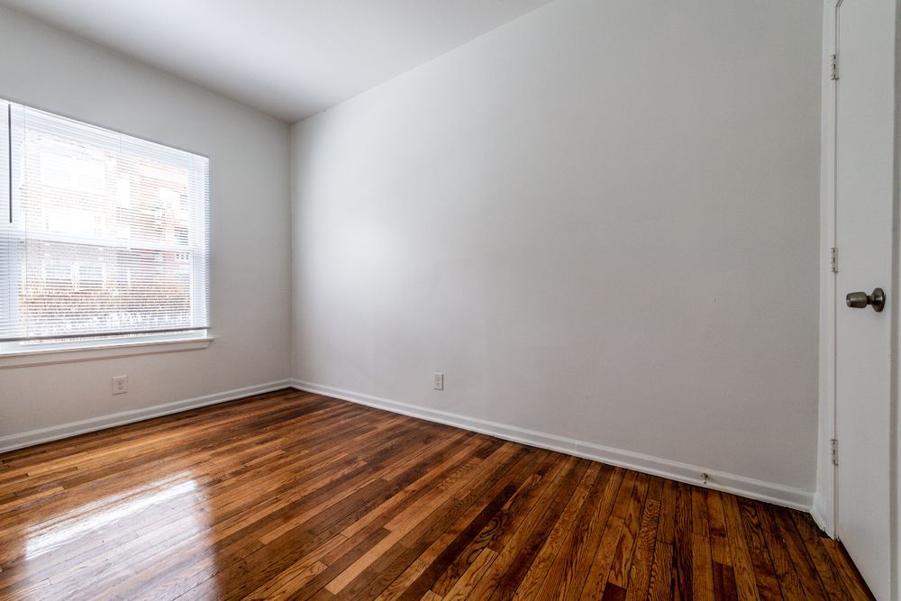 Empty room with wood floors, white walls, and a window with blinds.