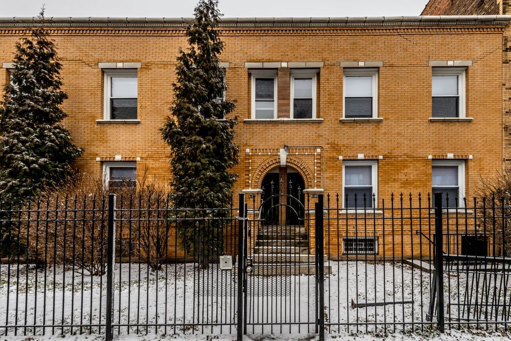 A two-story brick building with black fence and snow on the ground.