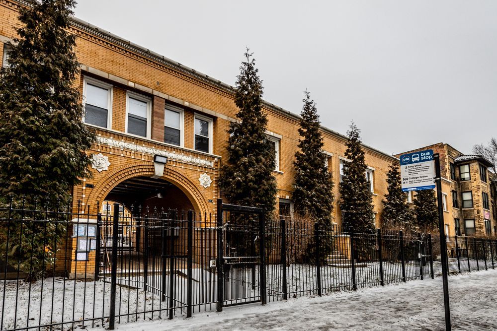 Brick school building with arched entrance and snow-covered ground, fenced in.