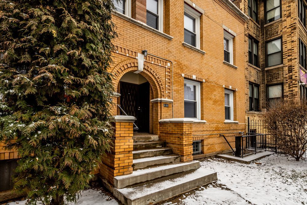 Yellow brick building with arched entryway and stairs covered in snow.