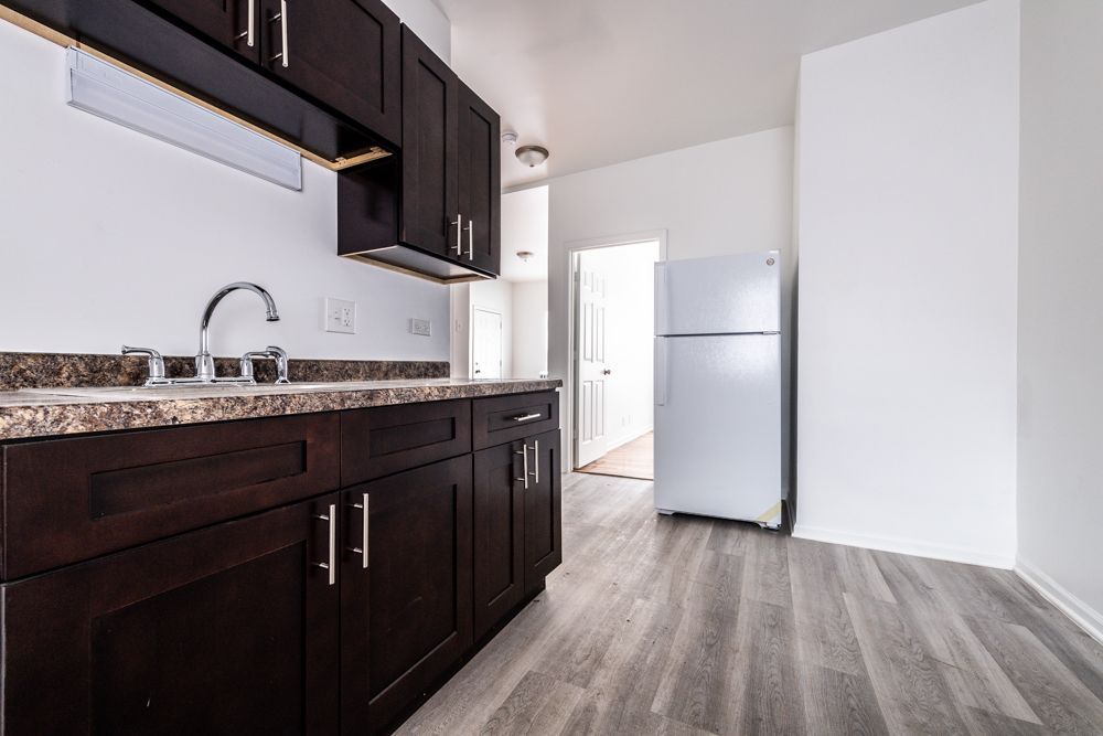Kitchen with dark cabinets, gray countertops and flooring, and a white refrigerator.