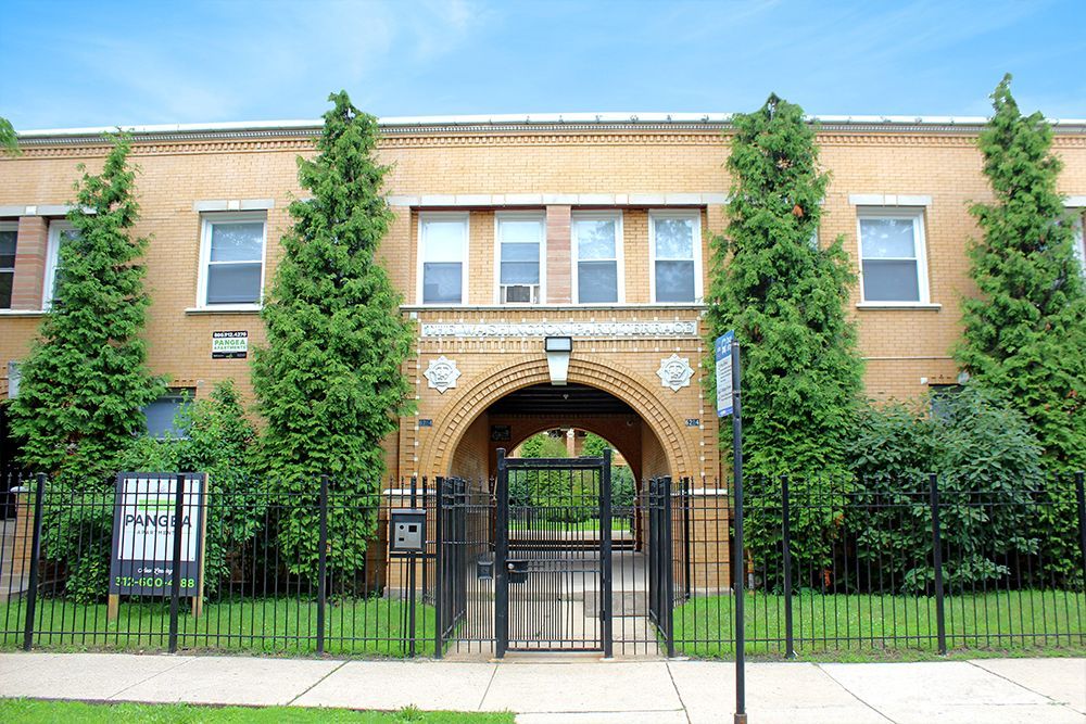 Yellow brick apartment building with arched entrance and black iron gate.