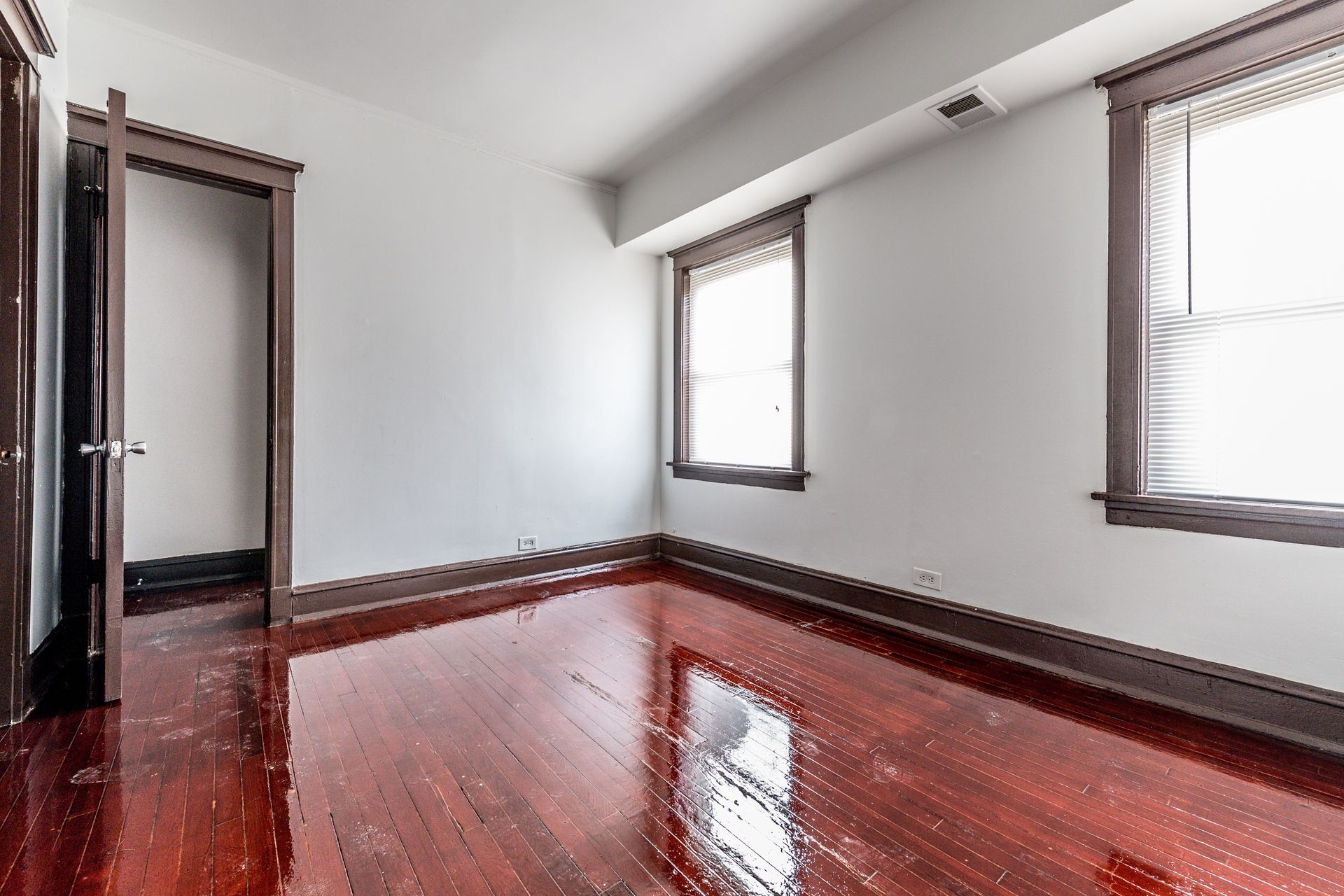 Empty room with wood floors and trim, white walls, and two windows.