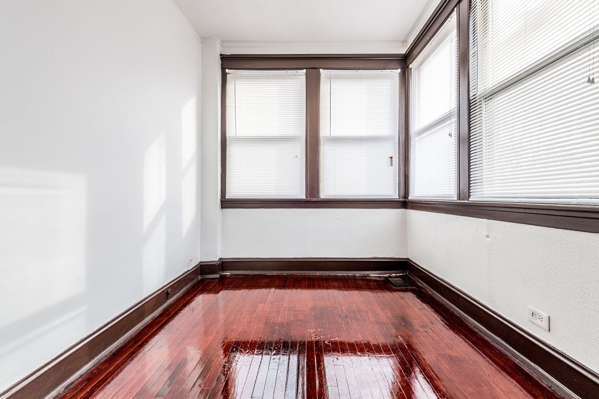 Empty room with wood floors and trim, white walls, and three windows with blinds.