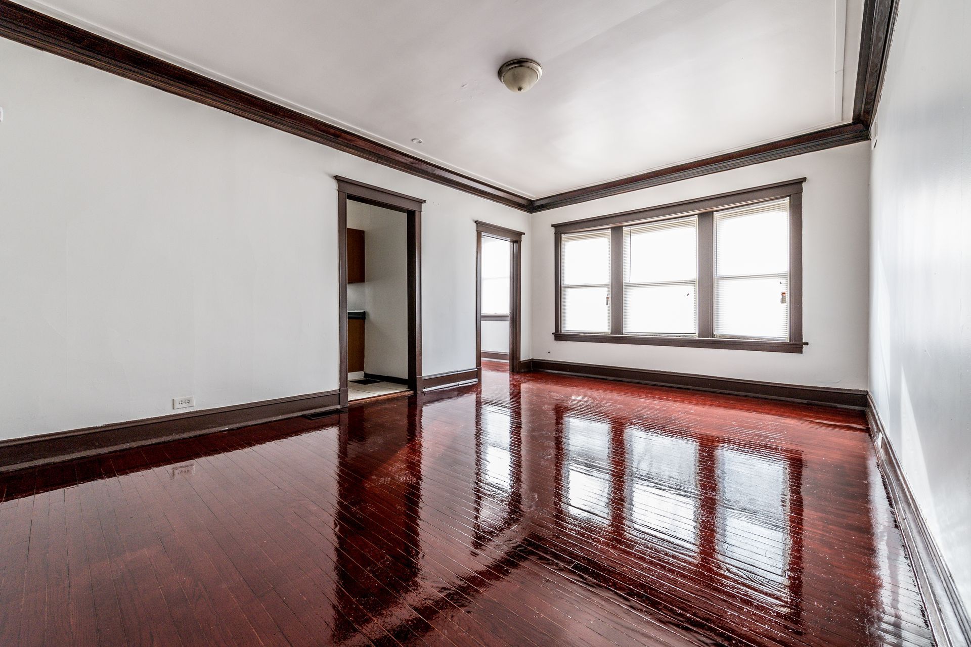 Empty room with dark wood trim, shiny red-brown floor, and bright windows reflecting light.